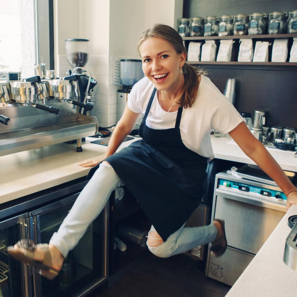 Young Caucasian barista laughing having fun jumping at work place